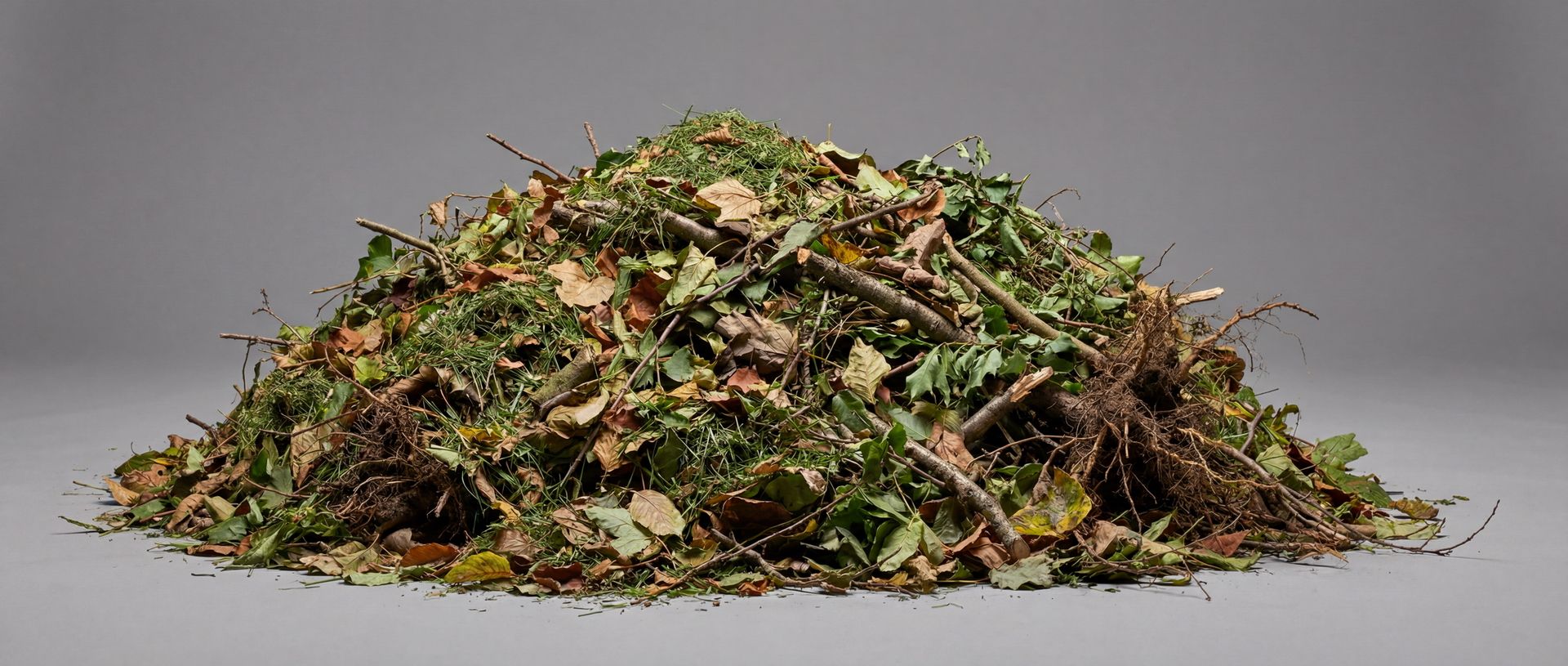 Ein Haufen loser Baum- und Strauchschnitt mit Laub, Rasenschnitt, Ästen und Wurzeln auf grauem Grund.