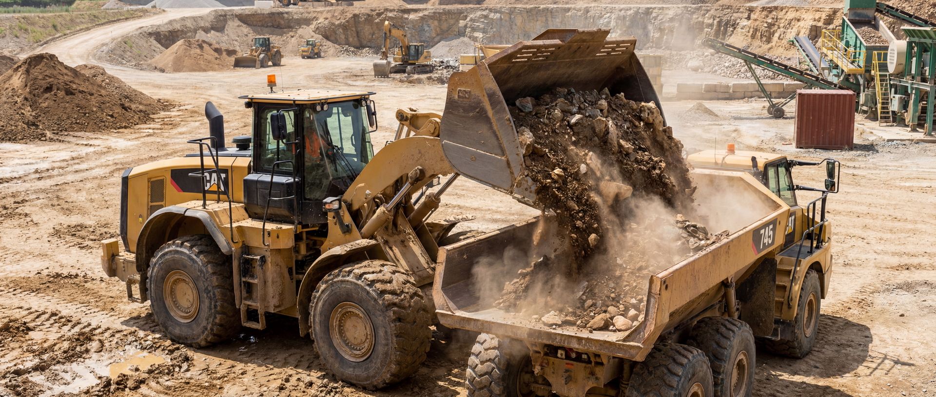 Ein gelber Radlader von CAT belädt einen Muldenkipper mit Gestein und Erde auf einer Baustelle.